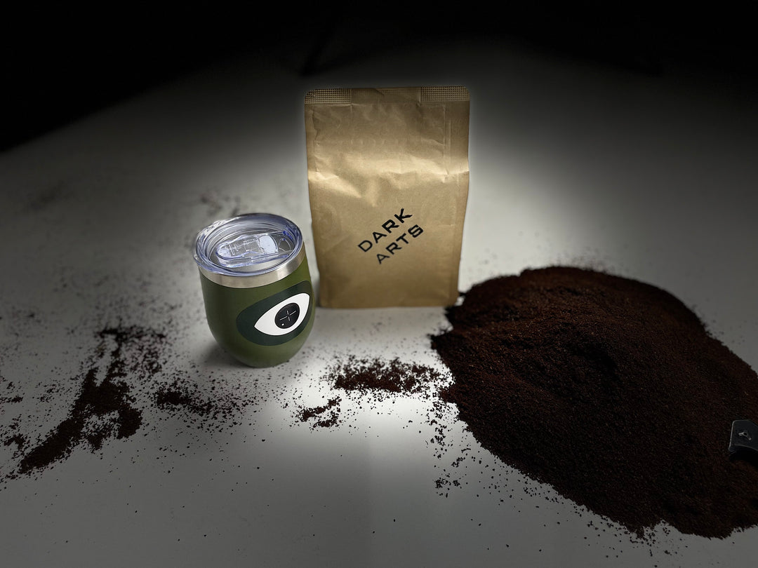Dark Arts coffee bag, a coffee tumbler with logo, and a large pile of ground coffee with dramatic lighting.