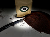Dark Arts coffee bag with a pile of ground coffee and a knife placed next to it, with dramatic lighting.