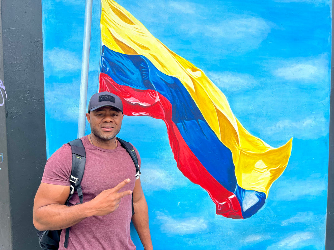 Man standing in front of a mural with the Colombian flag, making a peace sign.