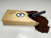 Opened 'DARK ARTS' coffee bag with ground coffee spilling out and a black knife placed inside the opening.